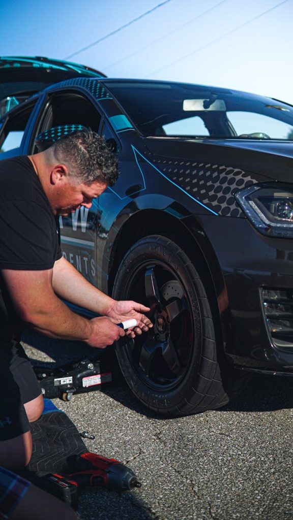 A man fixing a car tire on the road with tools, showcasing auto repair service.