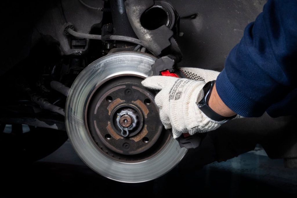 Mechanic working on car brake system in a workshop setting.